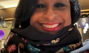 Nicki Fogle wearing a colorful scarf. They have brown skin, dark eyes and black hair